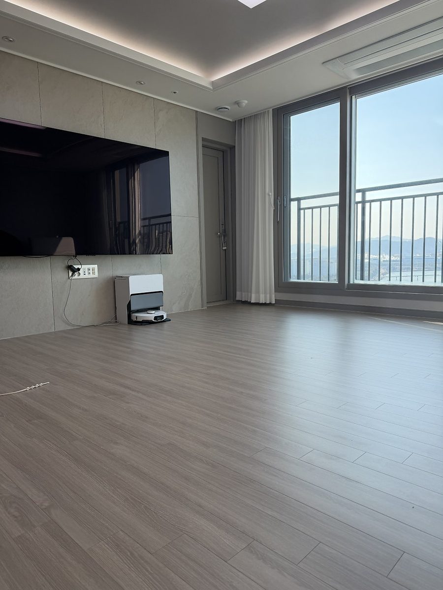 창가까지 갈색 나뭇결 마루가 깔린 거실과 벽걸이 TV